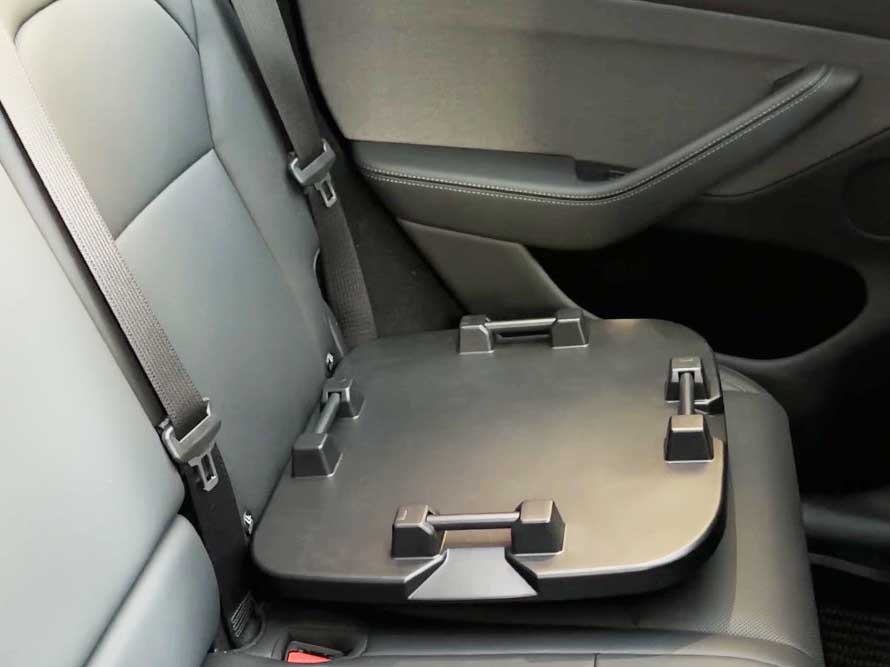 A black, rigid plastic ISOFIX pet safety seat base installed on a car's grey back seat, showing four connection points designed to allow a pet carrier to be attached in multiple orientations.