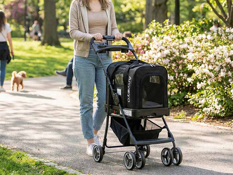 A woman in casual attire pushes a black Anvoya pet stroller with a black pet carrier