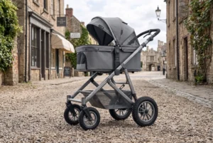 Gray baby stroller with sturdy wheels, parked on a cobblestone street in a historic village setting.