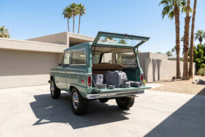 A vintage luxury off-road vehicle parked on a bright, minimalist concrete driveway under a clear blue sky.